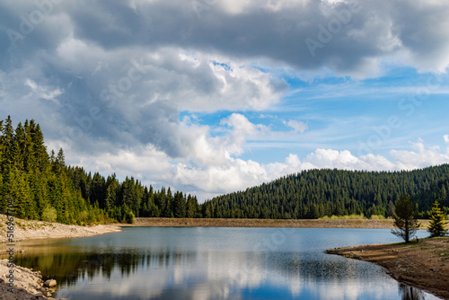 Fototapeta Naklejka Na Ścianę i Meble -  Lake with clear water and stone shore in spruce forest with fir trees against a daytime sky
