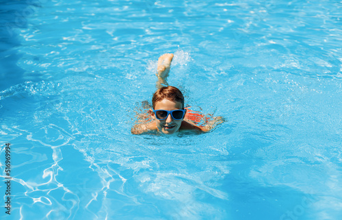 Boy in sunglasses swims in the pool, smiling and having a happy day. Cute happy little boy swims and dives in the pool