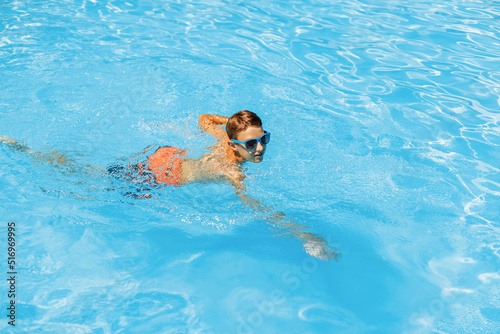 Boy in sunglasses swims in the pool, smiling and having a happy day. Cute happy little boy swims and dives in the pool
