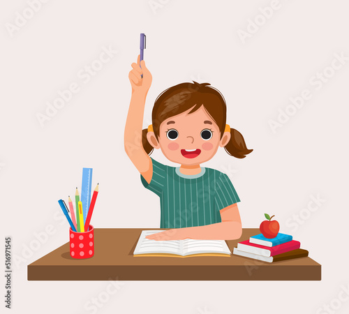 happy little girl student rising hand answering question sitting at her desk in the classroom