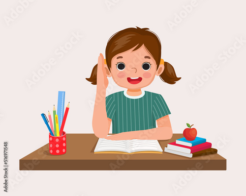 happy little girl student rising hand answering question sitting at her desk in the classroom