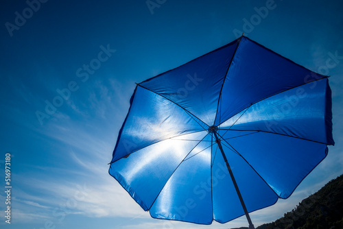 Vibrant blue beach umbrella against sun and clear sky