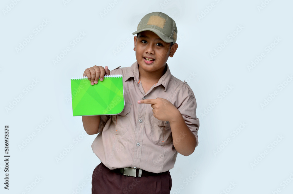 Asian boy in scouting uniform pointing at a green book, isolated white background Asian boy in scouting uniform pointing at a green book, isolated white background