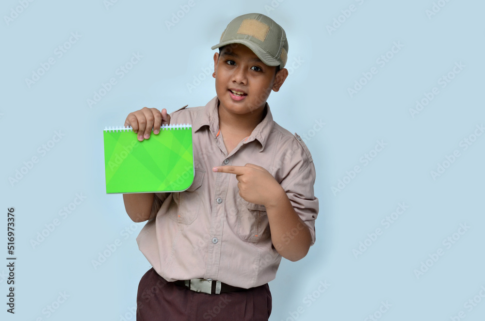 Asian boy in scouting uniform pointing at a green book, isolated white background Asian boy in scouting uniform pointing at a green book, isolated white background