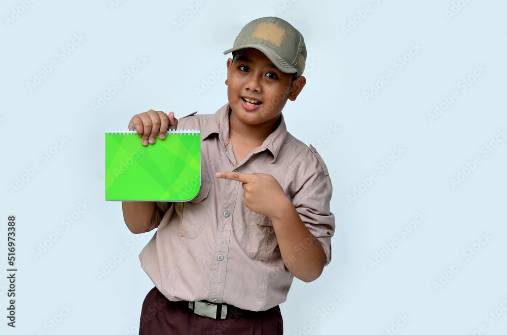 Asian boy in scouting uniform pointing at a green book, isolated white background Asian boy in scouting uniform pointing at a green book, isolated white background