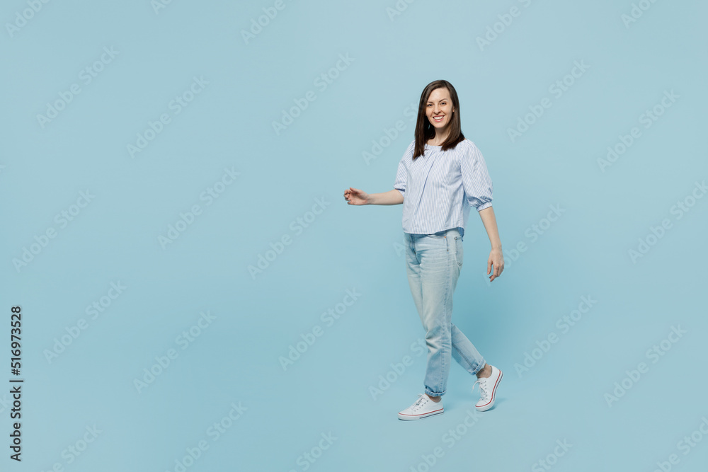 Full body side view young happy smiling cheerful woman she 20s wearing casual blouse walking strolling going isolated on pastel plain light blue background studio portrait. People lifestyle concept. Full body side view young happy smiling cheerful woman she 20s wearing casual blouse walking strolling going isolated on pastel plain light blue background studio portrait. People lifestyle concept.