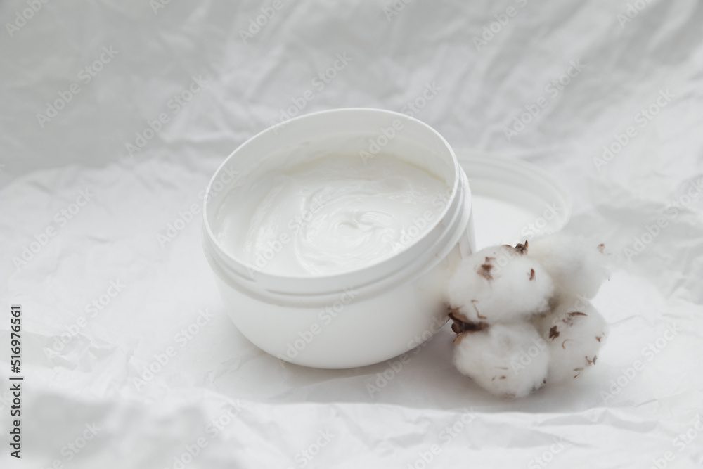Cream in white opened plastic jar and cotton bud on white crumpled paper background Cream in white opened plastic jar and cotton bud on white crumpled paper background