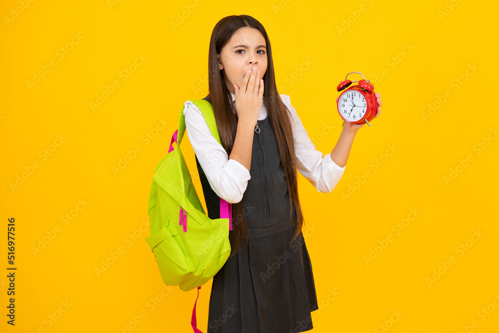 Back to school. Teenager school girl with backpack hold clock alarm, time to learn. School children on isolated yellow background. Tired and bored teenager girl. Back to school. Teenager school girl with backpack hold clock alarm, time to learn. School children on isolated yellow background. Tired and bored teenager girl.