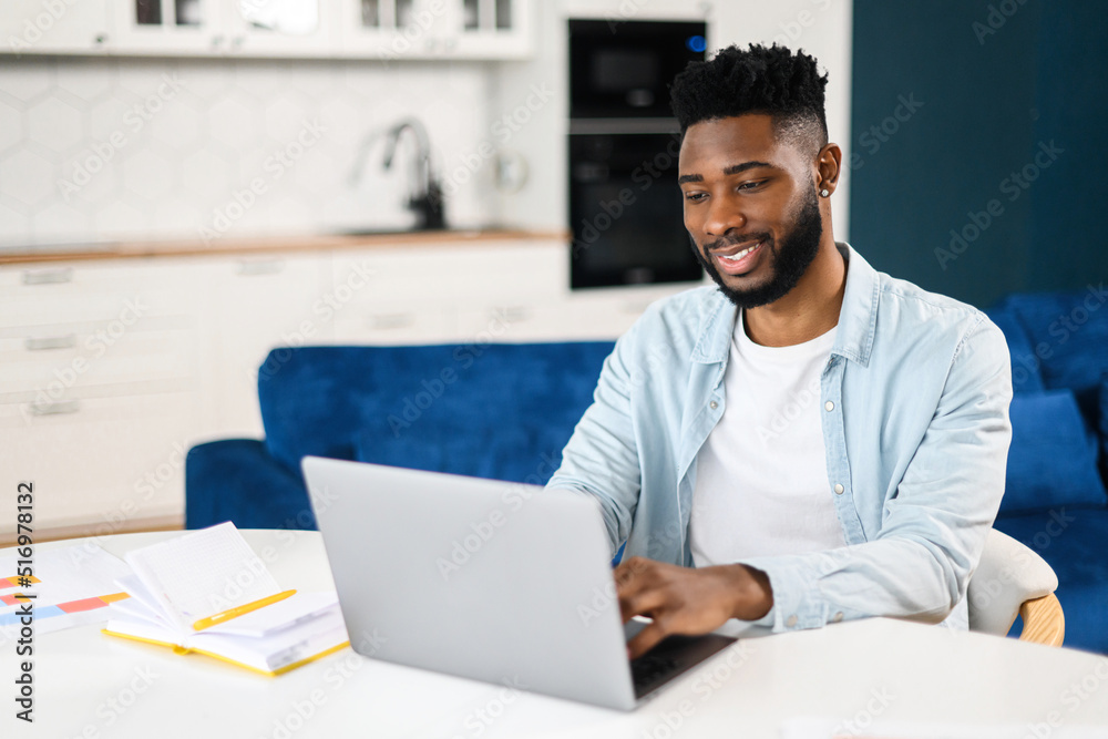 Mid adult multiracial man working in his home office, using laptop for communication with customers or colleagues. Smiling guy watching on computer screen with smile Mid adult multiracial man working in his home office, using laptop for communication with customers or colleagues. Smiling guy watching on computer screen with smile