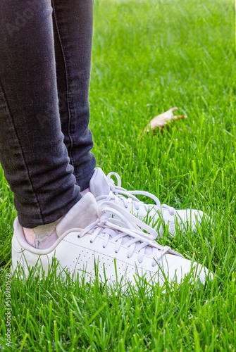 Women's legs in black jeans and white sneakers.
