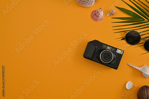 Top view of tropical palm leaf branches, sea shells and camera on yellow background with empty space for text. Travel vacation, Summer concept background.