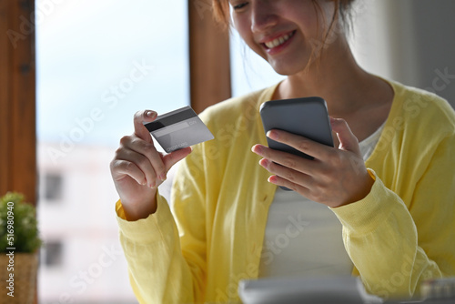 Close up of young businesswoman entering typing credit card number on smartphone, feeling excited to purchase items from an online store, order food, pay bills.