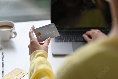 Back view of Asian woman in casual outfit entering typing credit card number on laptop to purchase items from an online store, order food, pay bills.