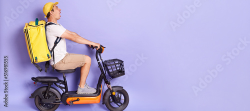 Side view full length portrait of courier man wearing with thermo backpack delivering food on electric scooter, looking ahead with scared expression, avoids accident, isolated over purple background