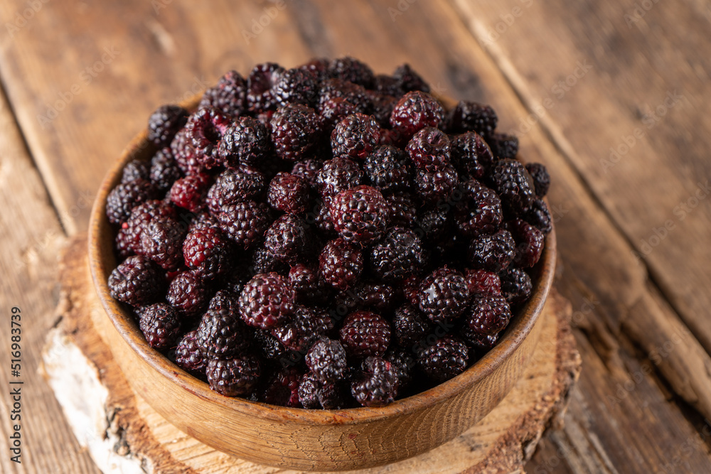 The black berry is a hybrid of raspberries and blackberries. Berries in a wooden bowl on the table. Vitamin summer food. Harvest. Raspberry and blackberry. Black raspberry. The black berry is a hybrid of raspberries and blackberries. Berries in a wooden bowl on the table. Vitamin summer food. Harvest. Raspberry and blackberry. Black raspberry.