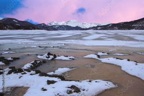 Winter view of lake campotosto and in the background the mountains area of gran sasso italy during sunset