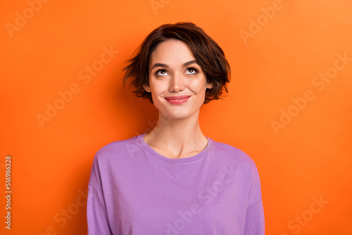 Photo of adorable thoughtful girl dressed purple pullover looking up empty space isolated orange color background photo