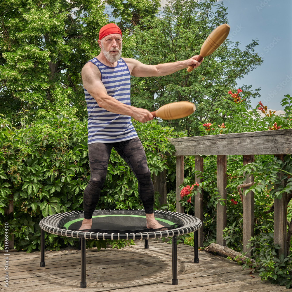 senior man is exercising on a mini trampoline with wooden Indian clubs in a backyard patio fitness and rebounding concept Stock Photo Adobe Stock