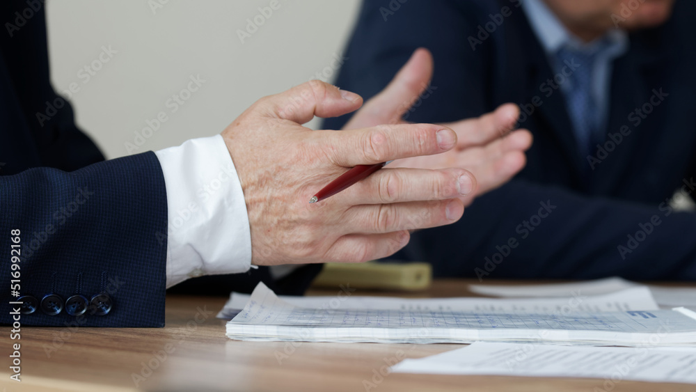Hand of man with pen, gesturing on the table next to documents. Age official, boss, lawyer or businessman. Participation in the meeting and signing of documents. No face. Selective focus. Hand of man with pen, gesturing on the table next to documents. Age official, boss, lawyer or businessman. Participation in the meeting and signing of documents. No face. Selective focus.
