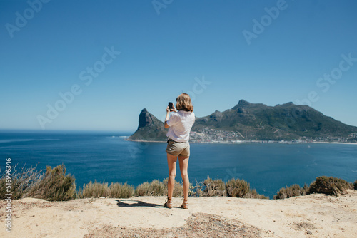 Young woman taking a photo on her phone at Chapmans peak coast