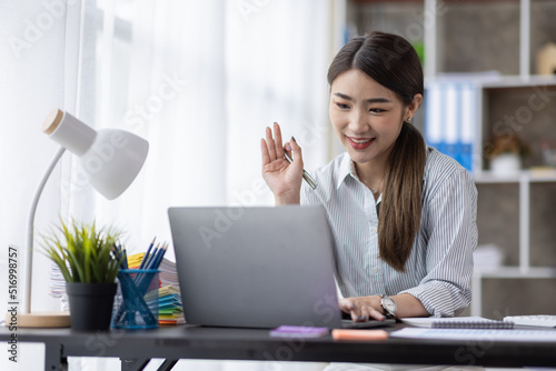 Young attractive business asian woman talking about sale report in video call conference on laptop computer online meeting in working from home office. Work remotely and Social isolation concept.