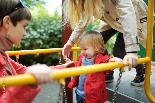 Cute toddler boy having fun with his big sisters on a playground outdoors on warm autumn day.