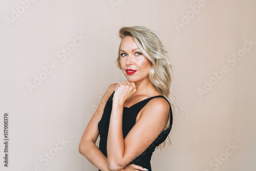 Portrait of gorgeous happy blonde young woman with bright makeup in evening dress on beige background