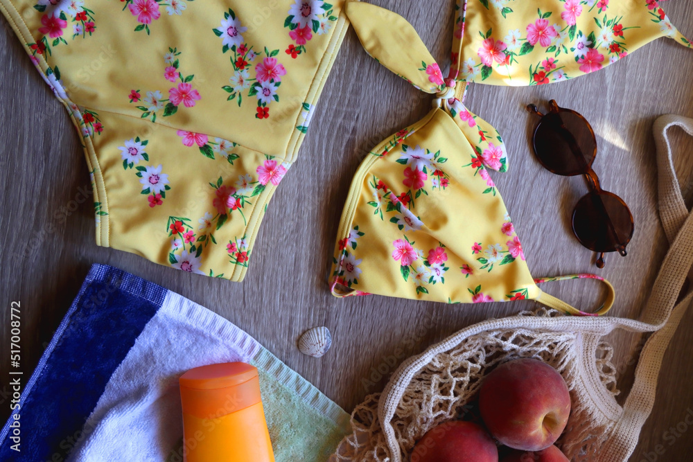 Striped towel, yellow floral swimming suit, sunglasses, mesh tote with fresh peaches, seashell and sunscreen. Beach essentials, flat lay. Striped towel, yellow floral swimming suit, sunglasses, mesh tote with fresh peaches, seashell and sunscreen. Beach essentials, flat lay.