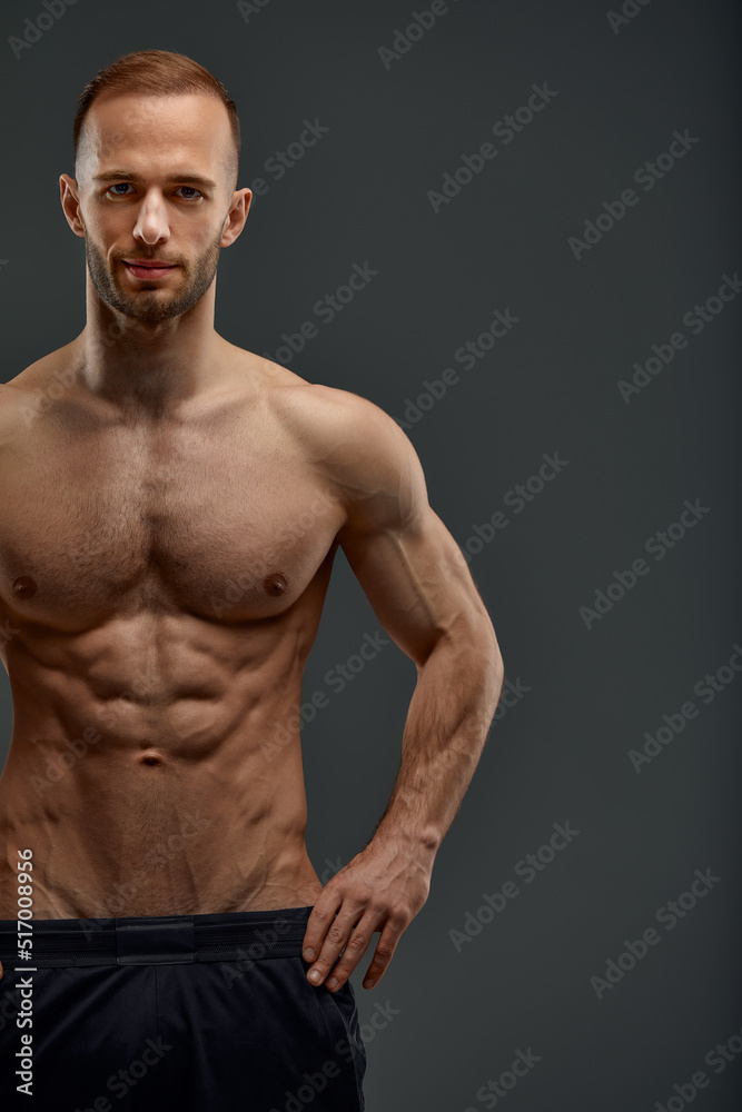 Obraz premium Croped shot of Young male athlete posing. Handsome athletic male power guy. Fitness muscular person. Young athlete showing muscles in the studio, posing shirtless on gray background.
