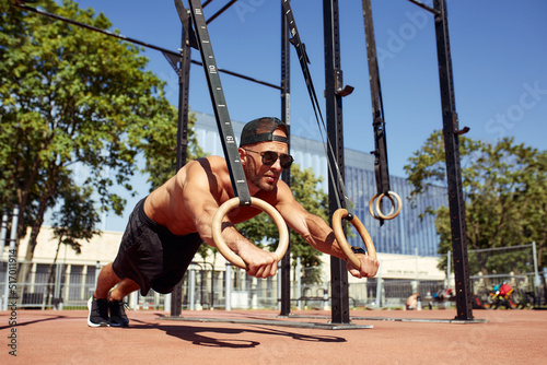 Muscular sportsman exercising on outdoor gymnastic rings in outdoor gym. Hands at rings dipping man doing exercise using rings