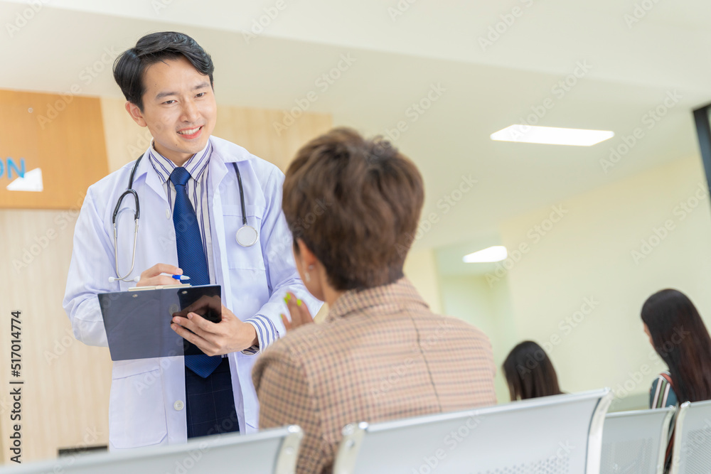 Fototapeta premium A handsome young Asian doctor in Thailand discussing the symptoms of a female patient attending the hospital.