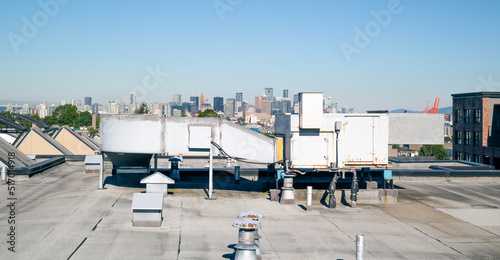 Hvac unit on flat roof with downtown skyline, vents and rooftop hatches and blue sky. Rooftop make-up air unit or packaged rooftop unit on a residential or commercial strata building. Selective focus.