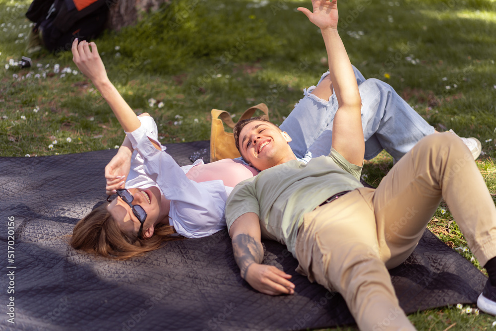 Top view of two friends lying down in a park and laughing. Close up of couple lying down outdoors enjoying the warm sun