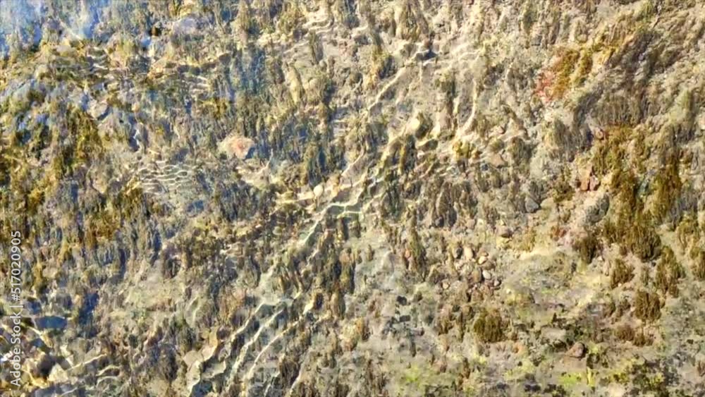 Water flows over surface of old stone overgrown with muloi and silt on sunny day. Ripples on surface of water and reflections of blue sky on mirror surface. Water flow. Natural abstract background Water flows over surface of old stone overgrown with muloi and silt on sunny day. Ripples on surface of water and reflections of blue sky on mirror surface. Water flow. Natural abstract background