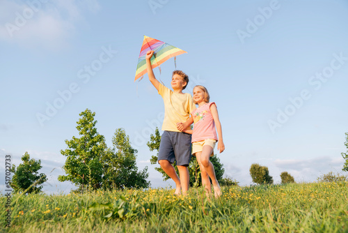 Brother and sister with a kite walking on the green grass. #517022733