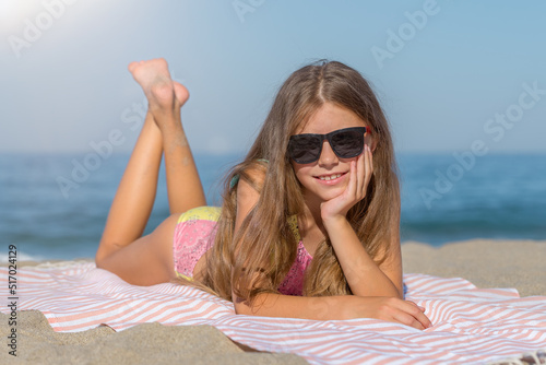 A teenage girl in a swimsuit and glasses lies on the beach.