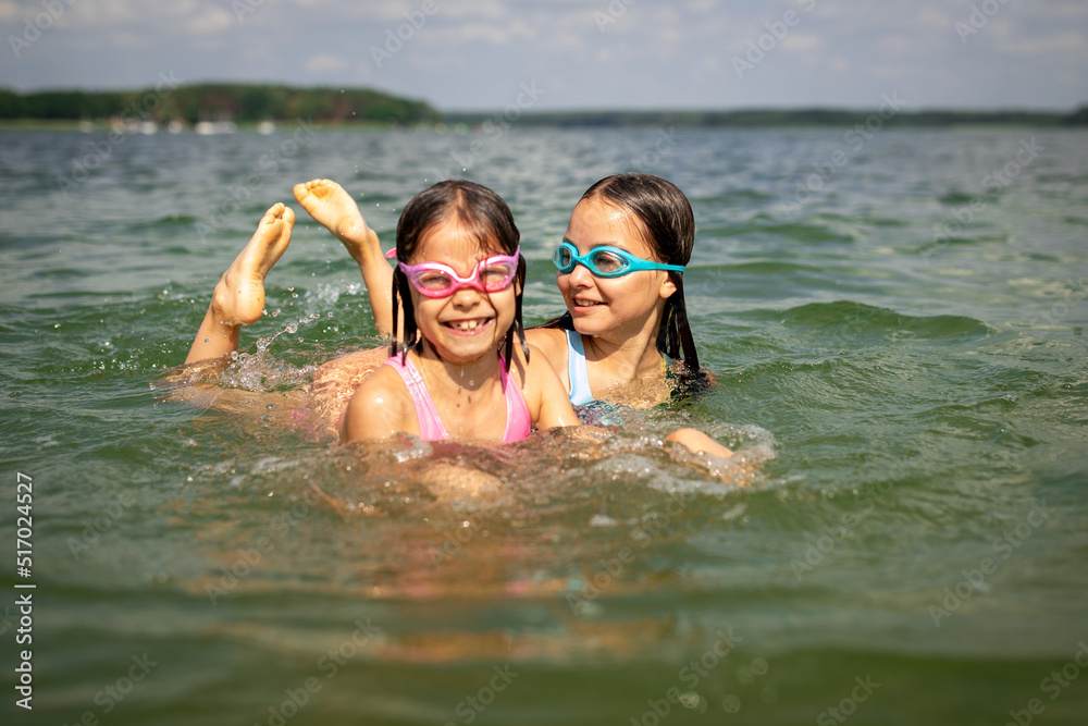 Two girls sisters swimming together in water and smiling on summer sunny day Two girls sisters swimming together in water and smiling on summer sunny day
