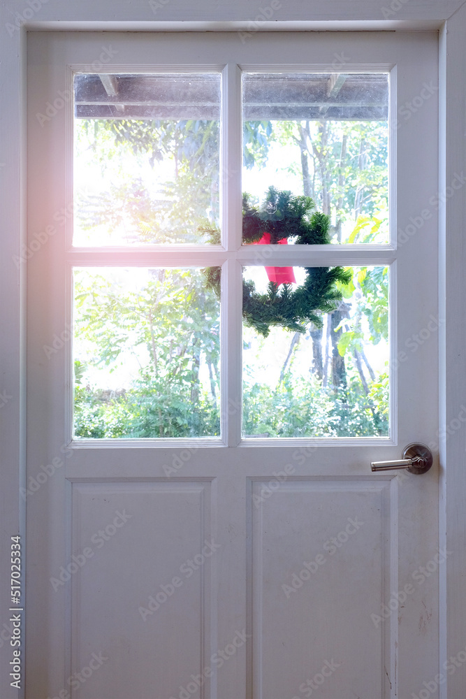 Fototapeta premium White wood door with glass window design and a flower crown decorated at the outside side to the green garden