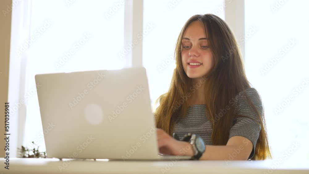 Happy girl student sits at a laptop. Online learning communication using keyboard. Typing in the office at the table. E-learning for teenagers. Homework. Lifestyle with a laptop in hand. Email at work Happy girl student sits at a laptop. Online learning communication using keyboard. Typing in the office at the table. E-learning for teenagers. Homework. Lifestyle with a laptop in hand. Email at work
