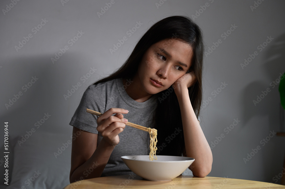 Young Asian woman feeling sad stress or lonely due to financial bankruptcy problem or economic recession crisis eating instant noodle alone in room. Personal business financial economy problem concept Young Asian woman feeling sad stress or lonely due to financial bankruptcy problem or economic recession crisis eating instant noodle alone in room. Personal business financial economy problem concept