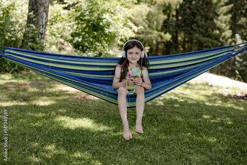 Mädchen, 8 Jahre, sitzt in einer Hängematte im Schatten und hört mit Kopfhörer Musik