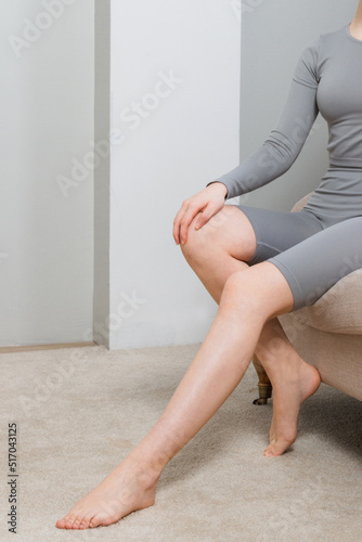 Long woman legs with smooth soft skin on sofa, couch or bed. A woman sits in a cozy home or apartment closeup. Woman doing skin care in the room. Beautiful sensual bare legs of a young woman.