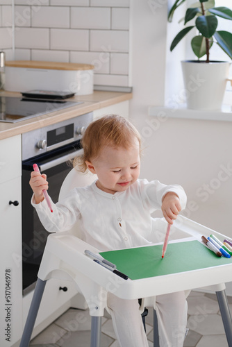 Left handed child. Toddler sitting on highchair drawing a picture using felt pens. Baby painting using colored markers.