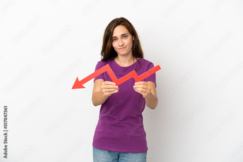 Young caucasian woman isolated on white background holding a downward arrow and with sad expression Young caucasian woman isolated on white background holding a downward arrow and with sad expression