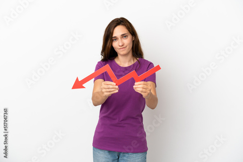 Young caucasian woman isolated on white background holding a downward arrow and with sad expression