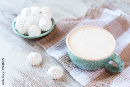 Ceramic bowl full of small meringue and cup of coffee on the kitchen towel on the wooden background. Copy space
