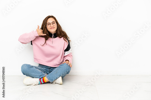 Young caucasian woman sitting on the floor isolated on white background making phone gesture. Call me back sign