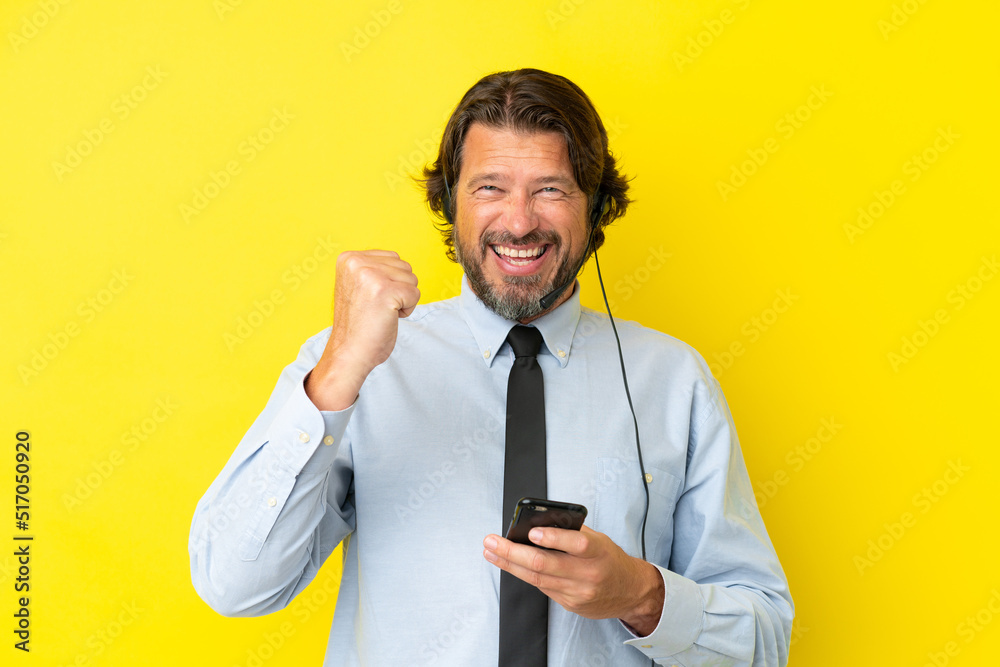 Telemarketer dutch man working with a headset isolated on yellow background with phone in victory position