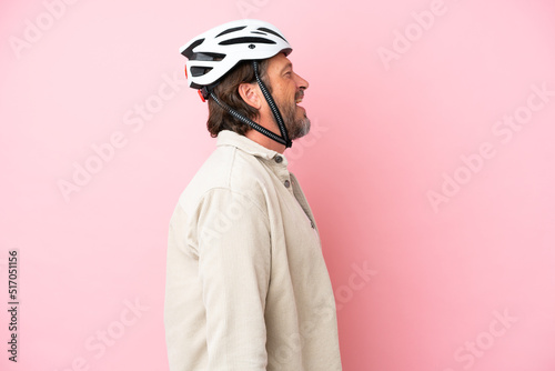 Senior dutch man with bike helmet isolated on pink background laughing in lateral position