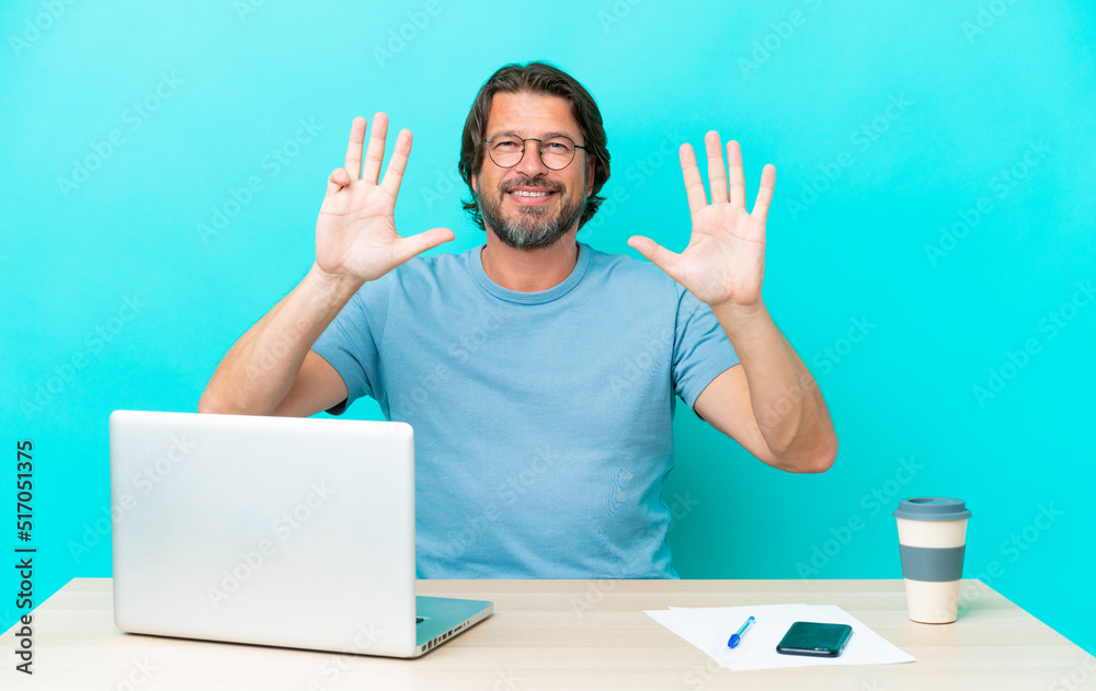 Senior dutch man in a table with a laptop isolated on blue background counting nine with fingers